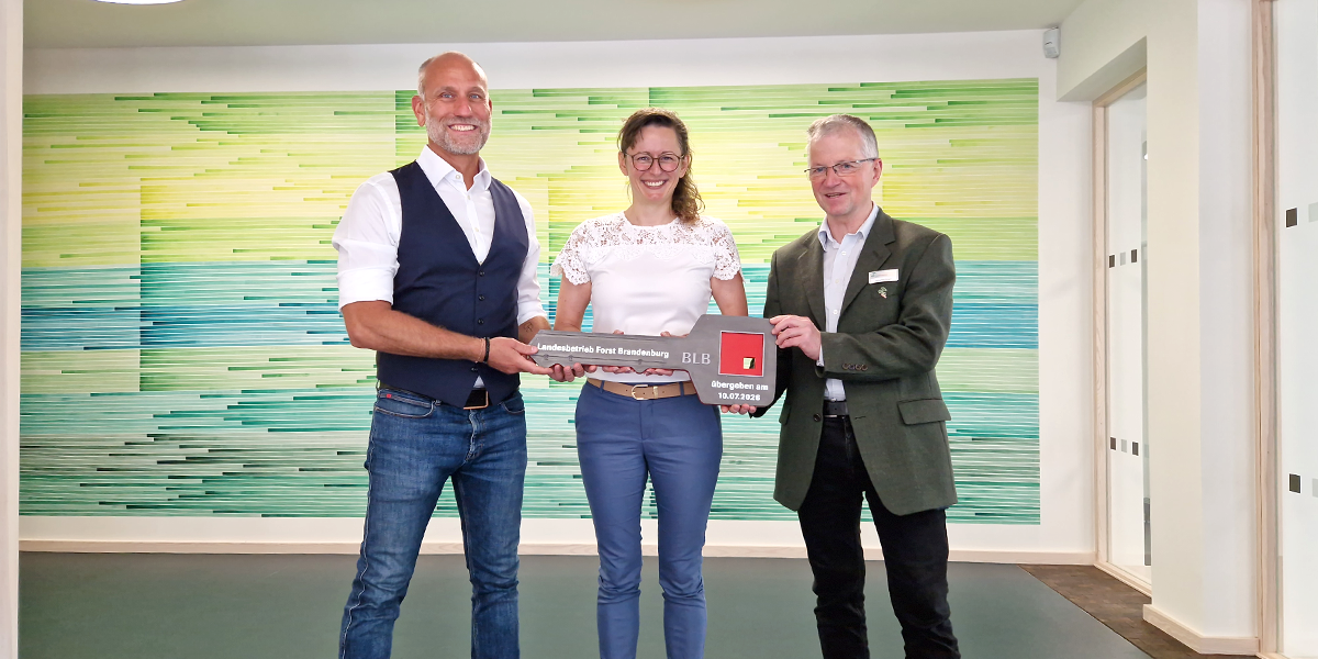 Drei Personen stehen nebeneinander und halten einen symbolischen Schlüssel in der Hand.