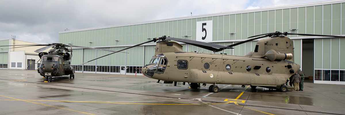Bild: Zwei Militärgubschrauber stehen vor einer großen Halle.