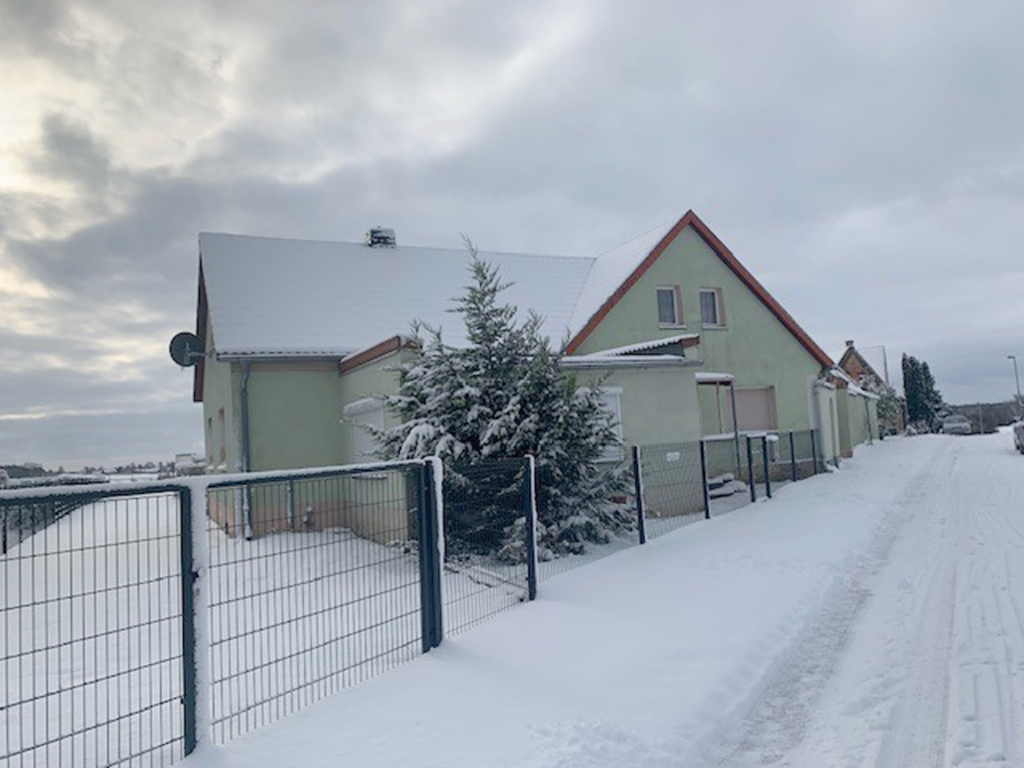 Giebelansicht eines großen Hauses mit lindt-grüner Fassade. Das Bild zeigt eine verschneite Winterlandschaft.