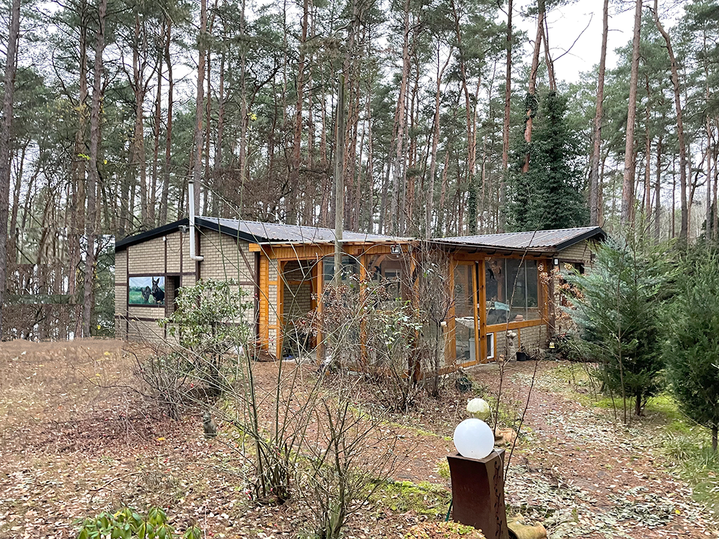 Ansicht eines kleinen Bungalows aus Backsteinen mit einem Vorbau aus Holz. 