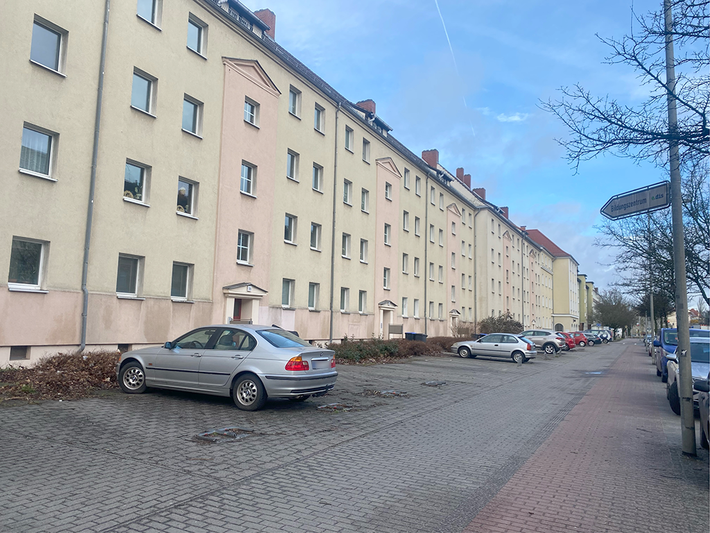 Blick auf einen Neubaublock. Davor parken vereinzelt Autos.