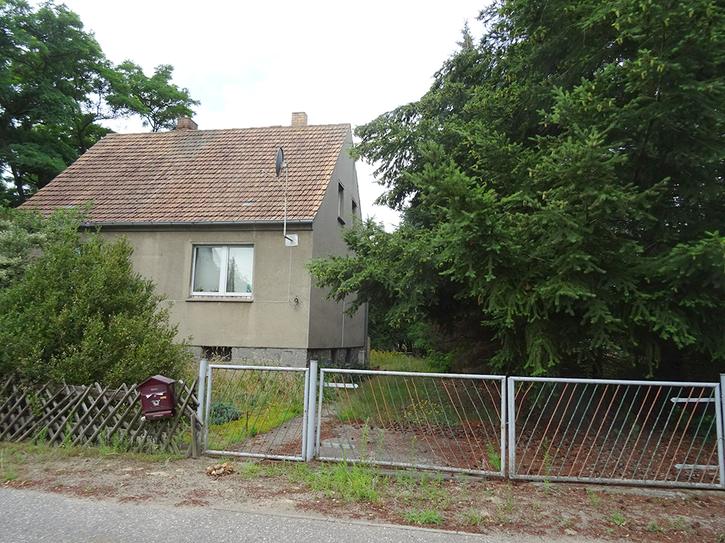 Ansicht eines zweistöckigen Hauses umgeben von viel Grün und einem Zaun.