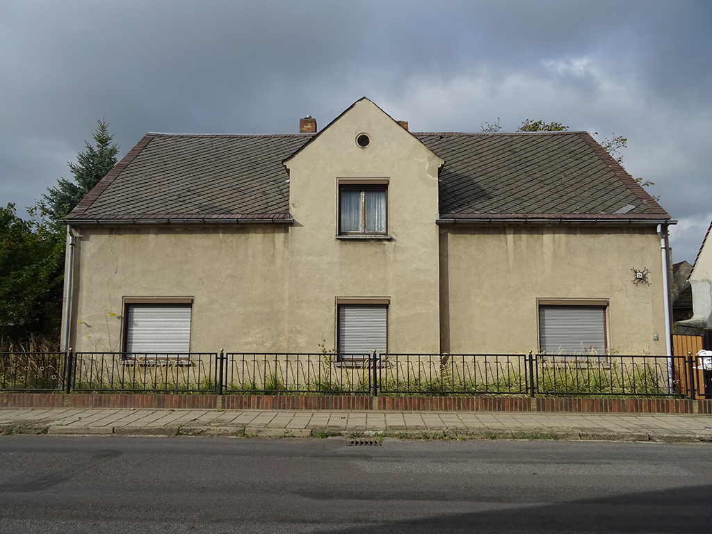 Ansicht eines zweistöckigen Hauses mit grauer Fassade und umgeben von einem Zaun.