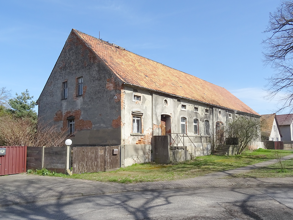 Straßenansicht eines älteren Hauses. Die Fassade ist grün und verwittert. Der Putz brökelt.