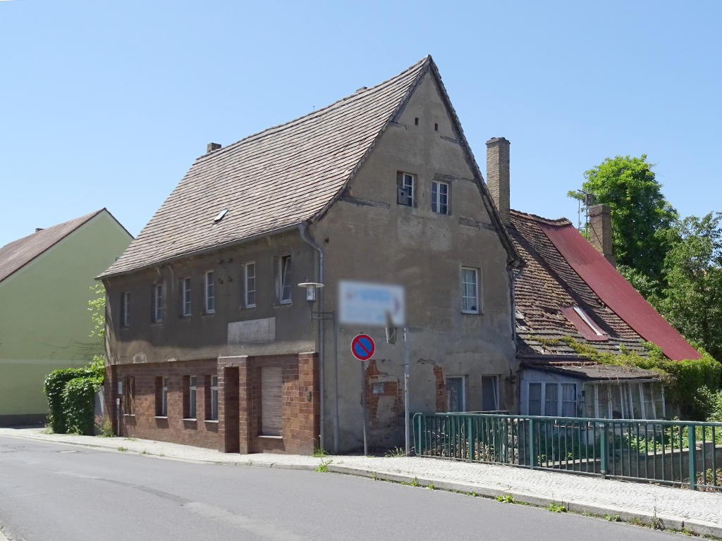 Giebelseite eines alten Hauses mit brökelndem Putz. Sockelleiste aus Backsteinen. Der Anbau ist in einem schlechten Zustand.