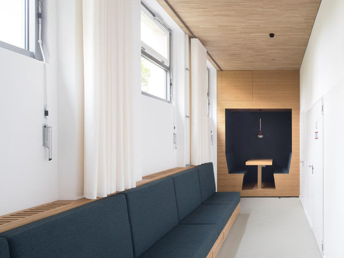 Blick in einen langen Flur. Unter den Souterrain-Fenstern ist eine lange dunkelbezogene Sitzbank. Am Ende eine Sitznische zum mobilen Arbeiten.