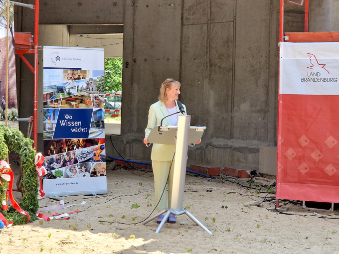 Frau in hellem Hosenanzug am Rednerpult.